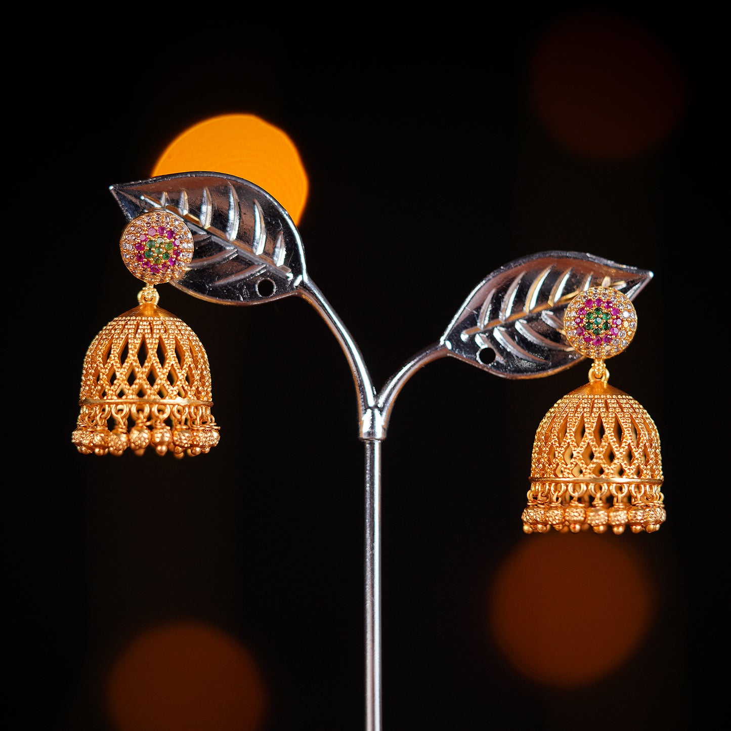 Gold jhumka earrings with intricate lattice design and pink gemstone accents.