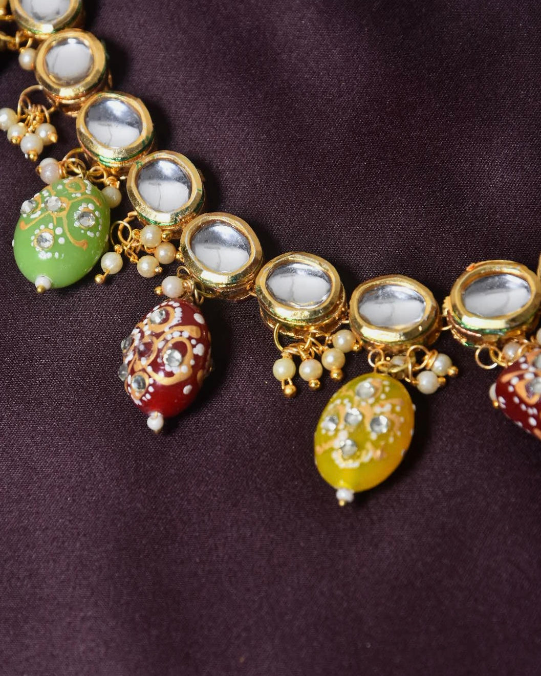 A close-up of a gold necklace with oval-shaped mirror embellishments and colorful, intricately designed beads hanging from it.