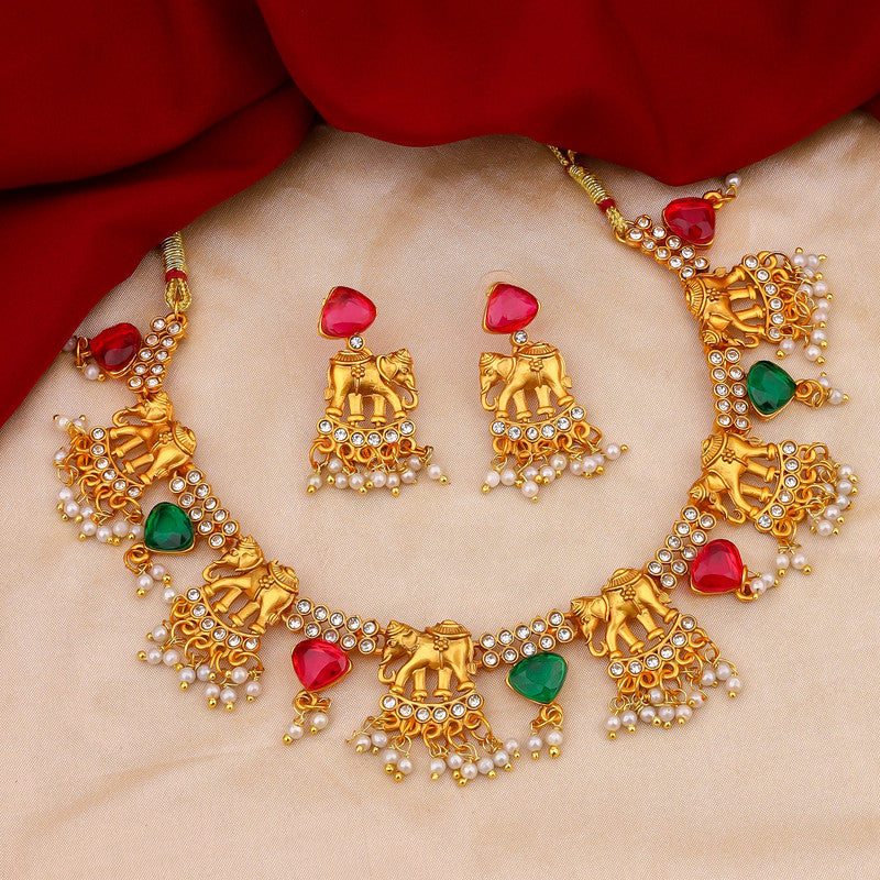 A gold necklace set with elephant motifs, red and green stones, and pearl accents, displayed on a beige fabric with a red cloth in the background.