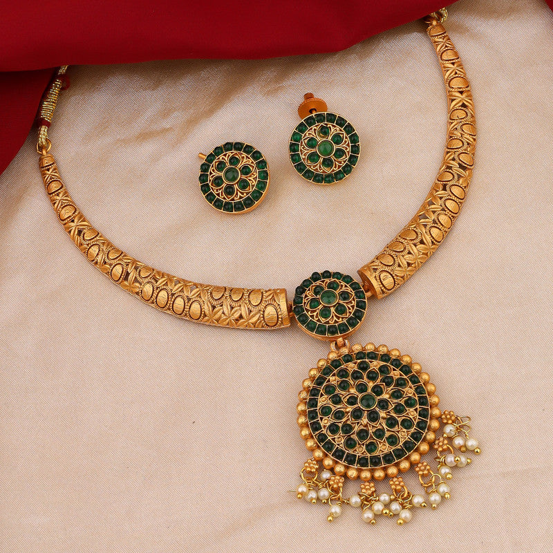 A gold necklace with intricate designs and green circular accents, accompanied by matching earrings, displayed on a beige fabric background.