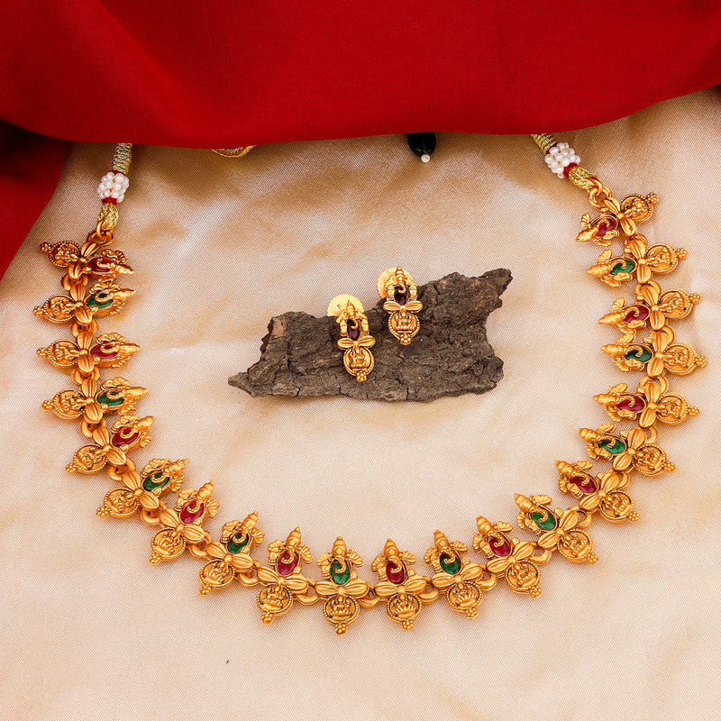 A gold necklace with intricate designs and matching earrings displayed on a beige fabric with a red cloth in the background.