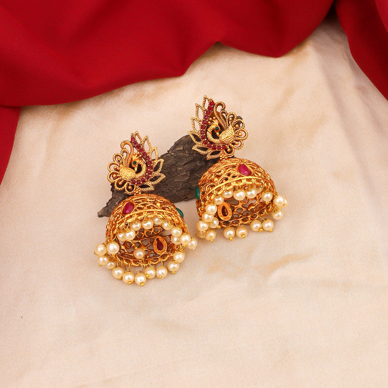 Gold jhumka earrings with intricate designs and pearl accents on a fabric background.