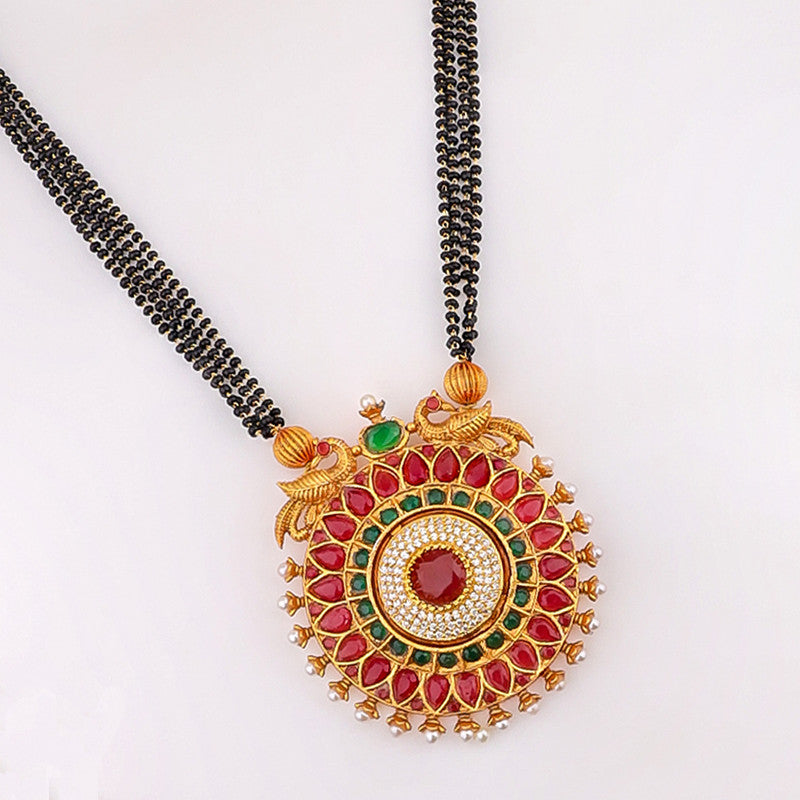 A traditional Indian necklace with a large circular pendant featuring red and green gemstones, intricate gold detailing, and a black beaded chain.