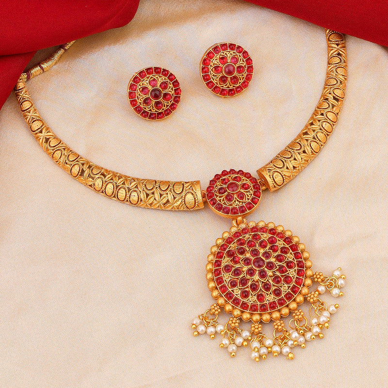 A gold necklace set with intricate red gemstone designs, including matching earrings, displayed on a beige fabric background.