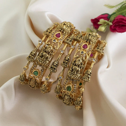 Two intricately designed gold bangles adorned with colorful gemstones and detailed carvings.