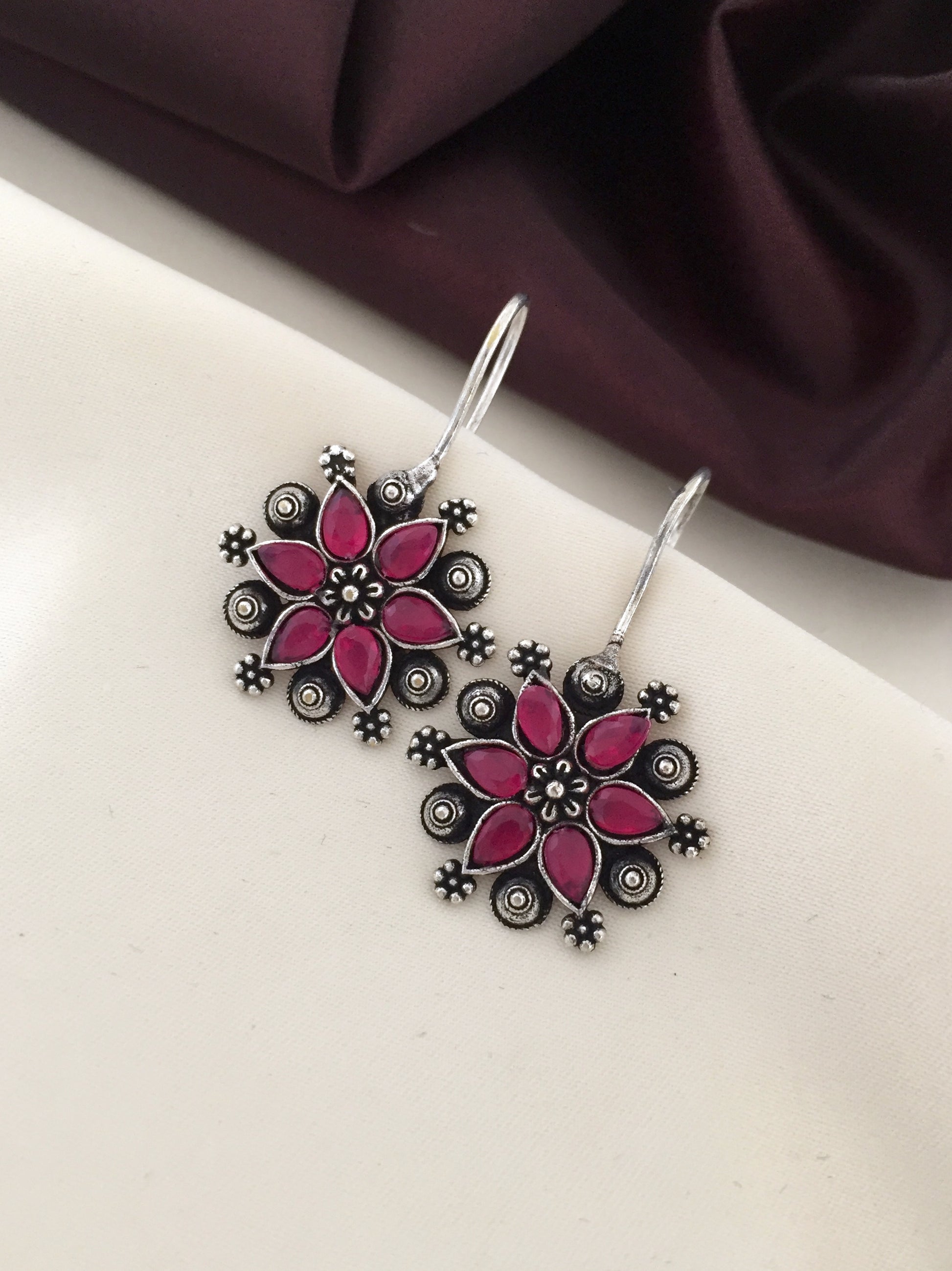 A pair of silver earrings with intricate floral designs and pink enamel accents.