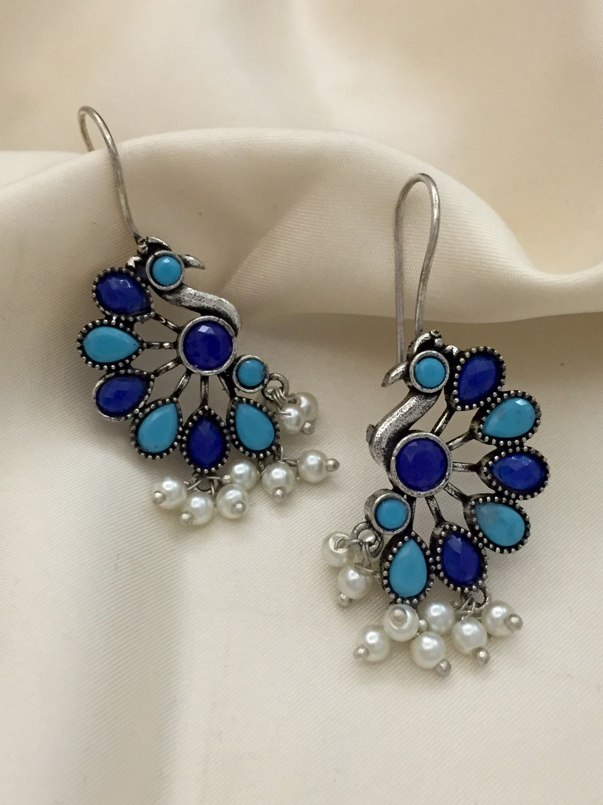 A pair of peacock-shaped earrings with blue and turquoise stones and dangling white pearls.