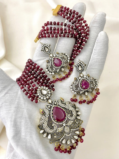 A set of jewelry featuring a necklace, earrings, and a pendant with red beads and intricate silver and gold detailing, adorned with red and white gemstones.