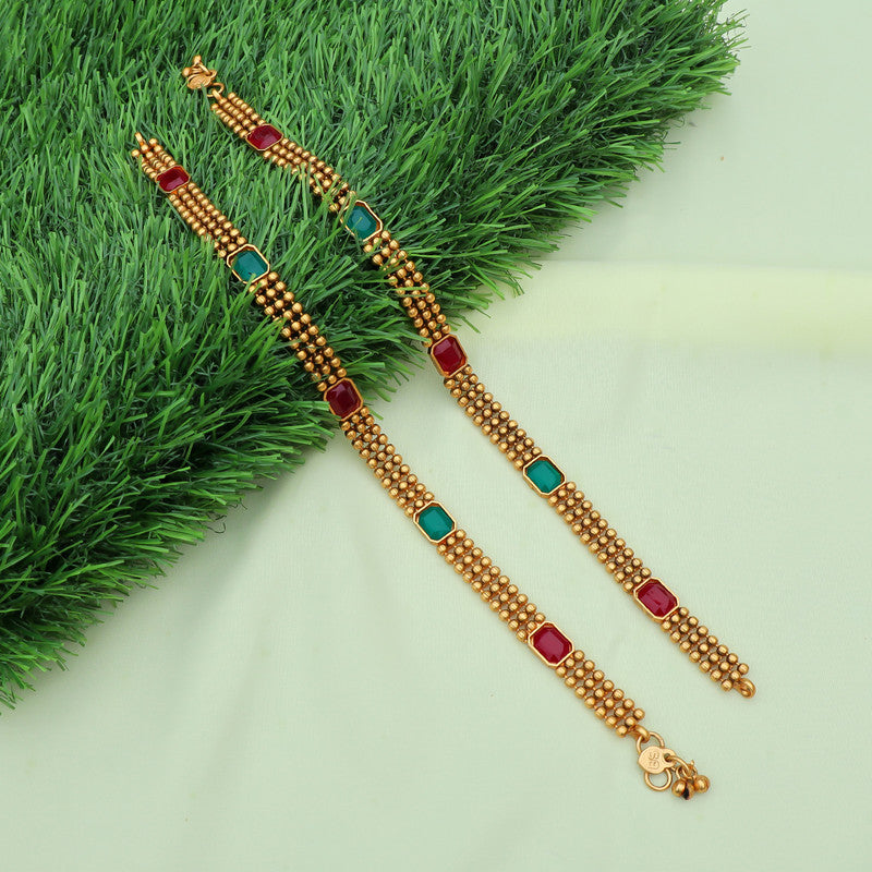 Traditional gold-plated anklets adorned with vibrant red and green stones, showcasing intricate craftsmanship and elegant design.