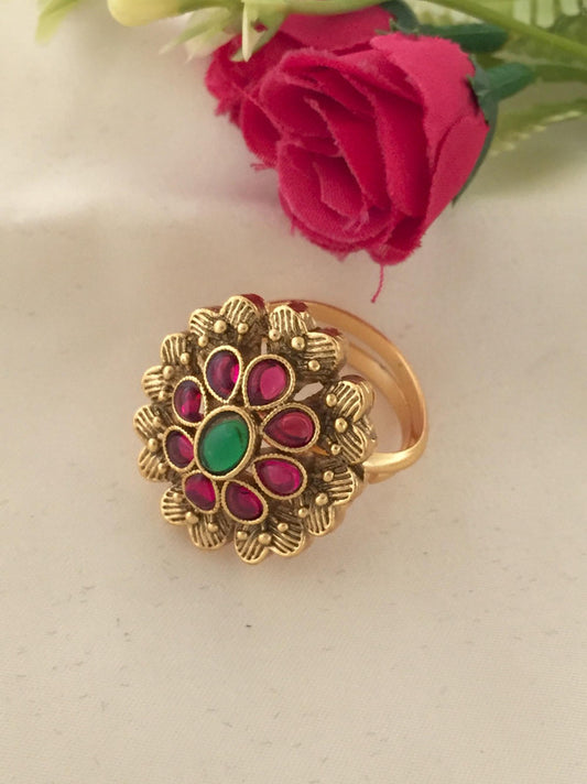 A gold ring with a floral design featuring red and green gemstones.