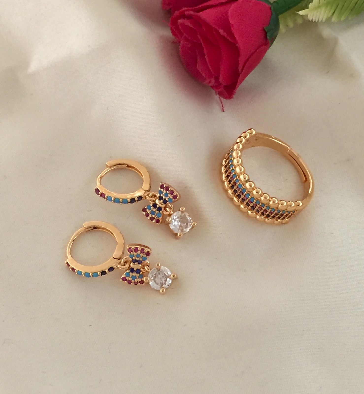 A set of gold hoop earrings with colorful gemstones and a matching gold ring with a row of gemstones.