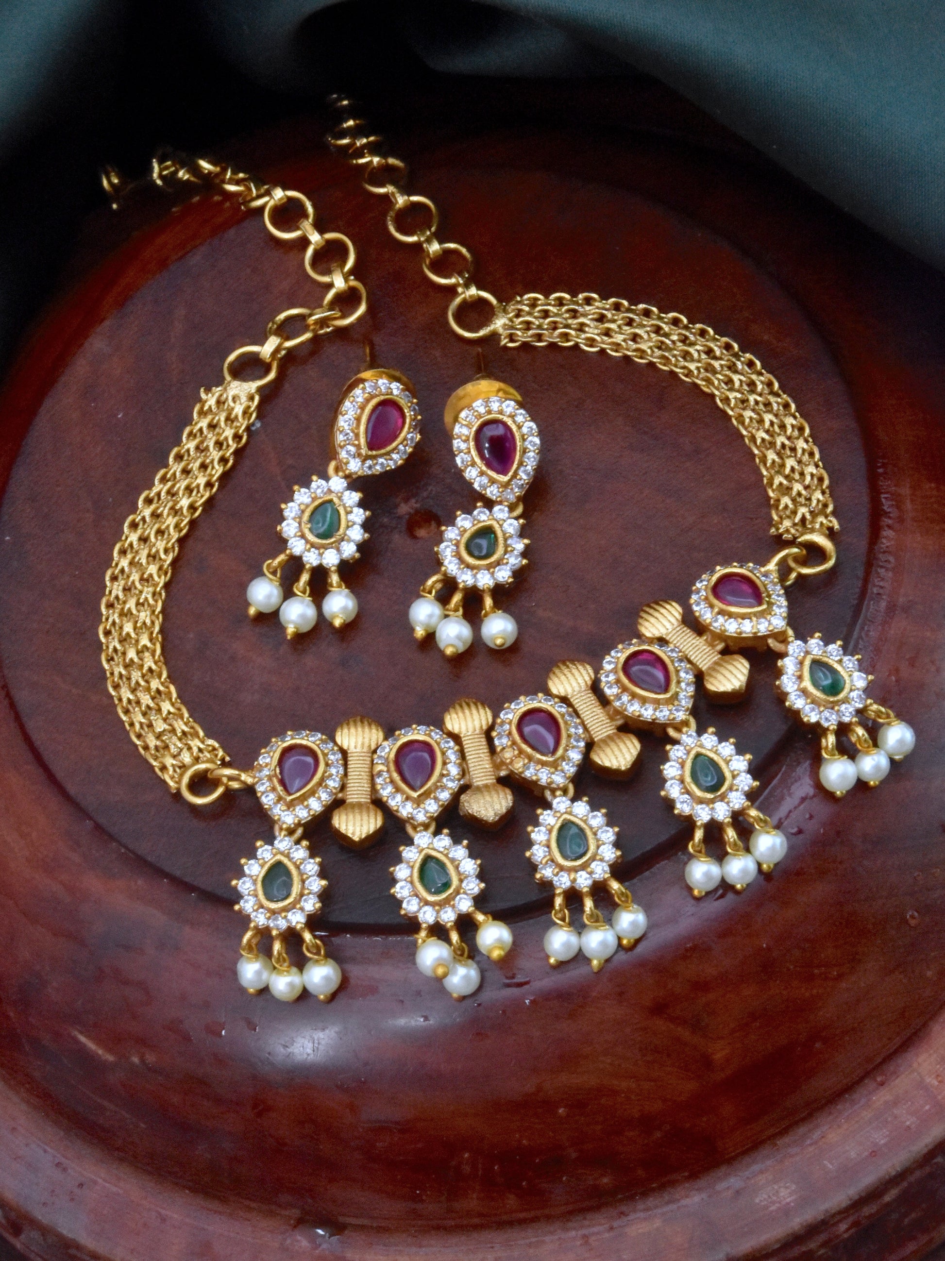 Gold necklace and earrings set with red and green gemstones and pearl accents.