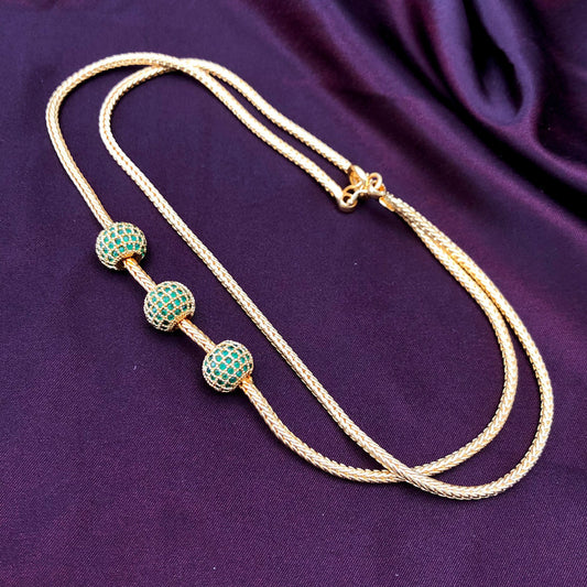 A gold necklace with three green beaded accents displayed on a dark purple fabric background.