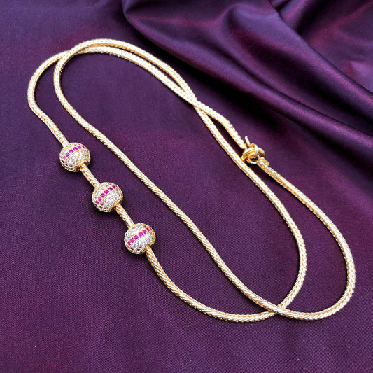 A gold necklace with three spherical beads encrusted with pink and white gemstones, displayed on a purple satin fabric background.