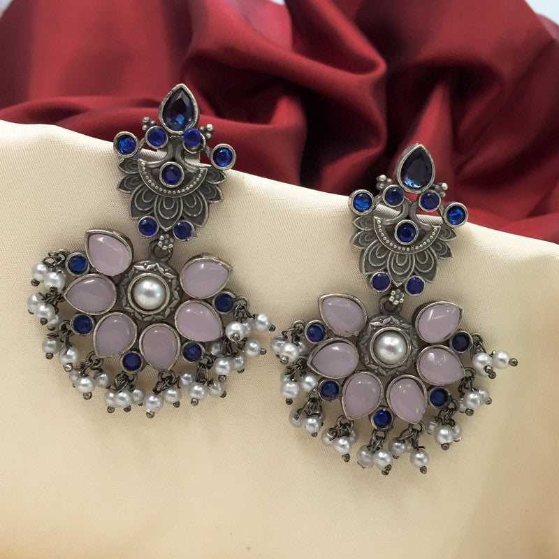 A pair of ornate silver earrings with blue and pink gemstones, featuring a floral design and small dangling pearls, displayed against a red and beige fabric background.