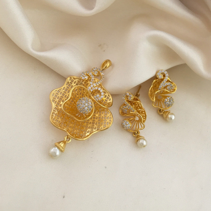 A set of gold jewelry consisting of a pendant and matching earrings, each adorned with intricate designs, small white stones, and pearl drops, displayed on a light fabric background.