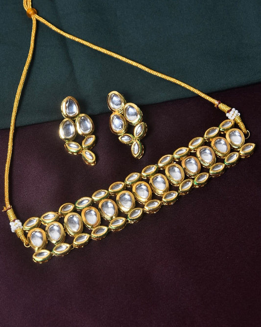 A gold choker necklace with matching earrings, featuring oval and teardrop-shaped white stones.