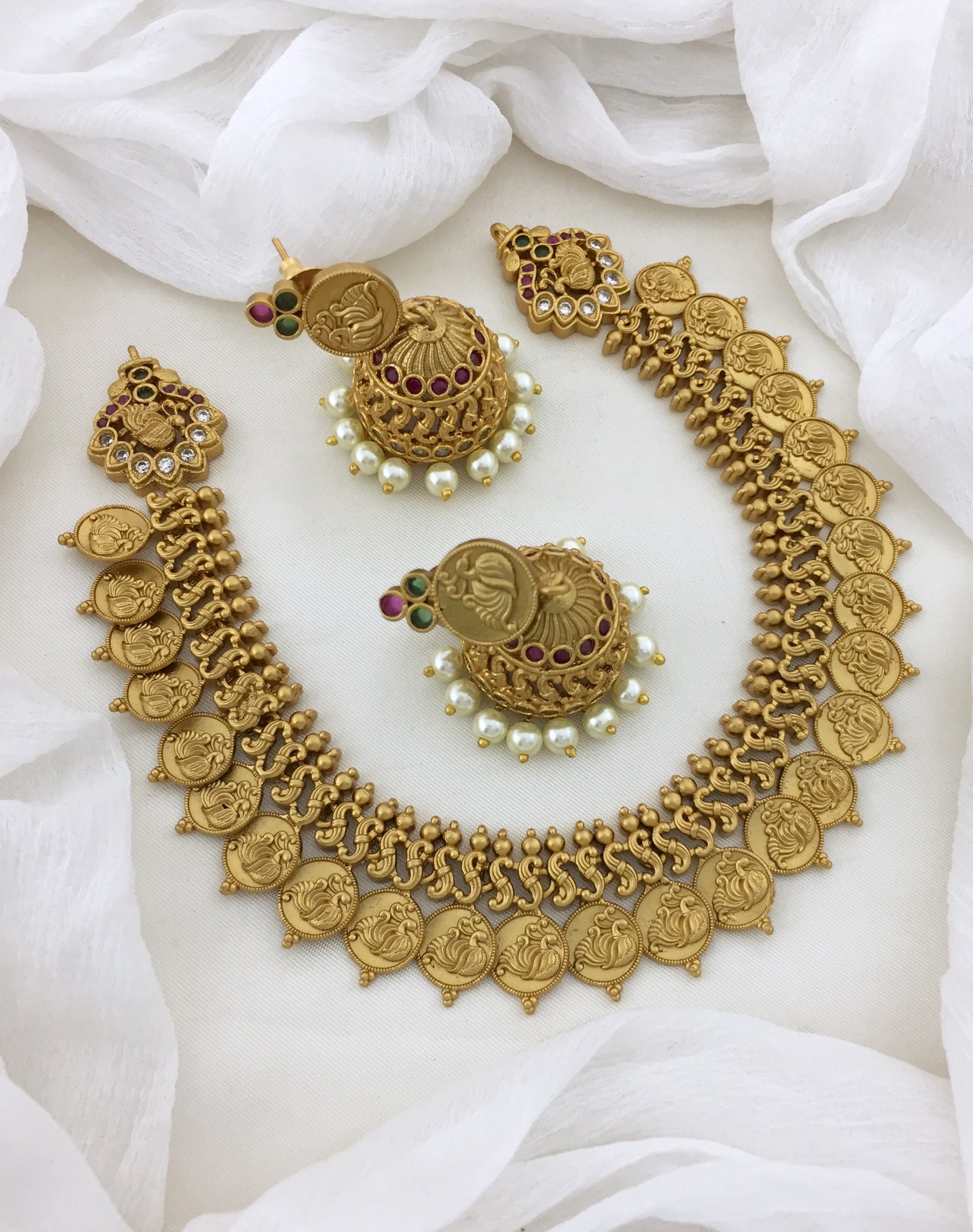 A gold necklace set with intricate designs and matching earrings adorned with pearls and red gemstones.