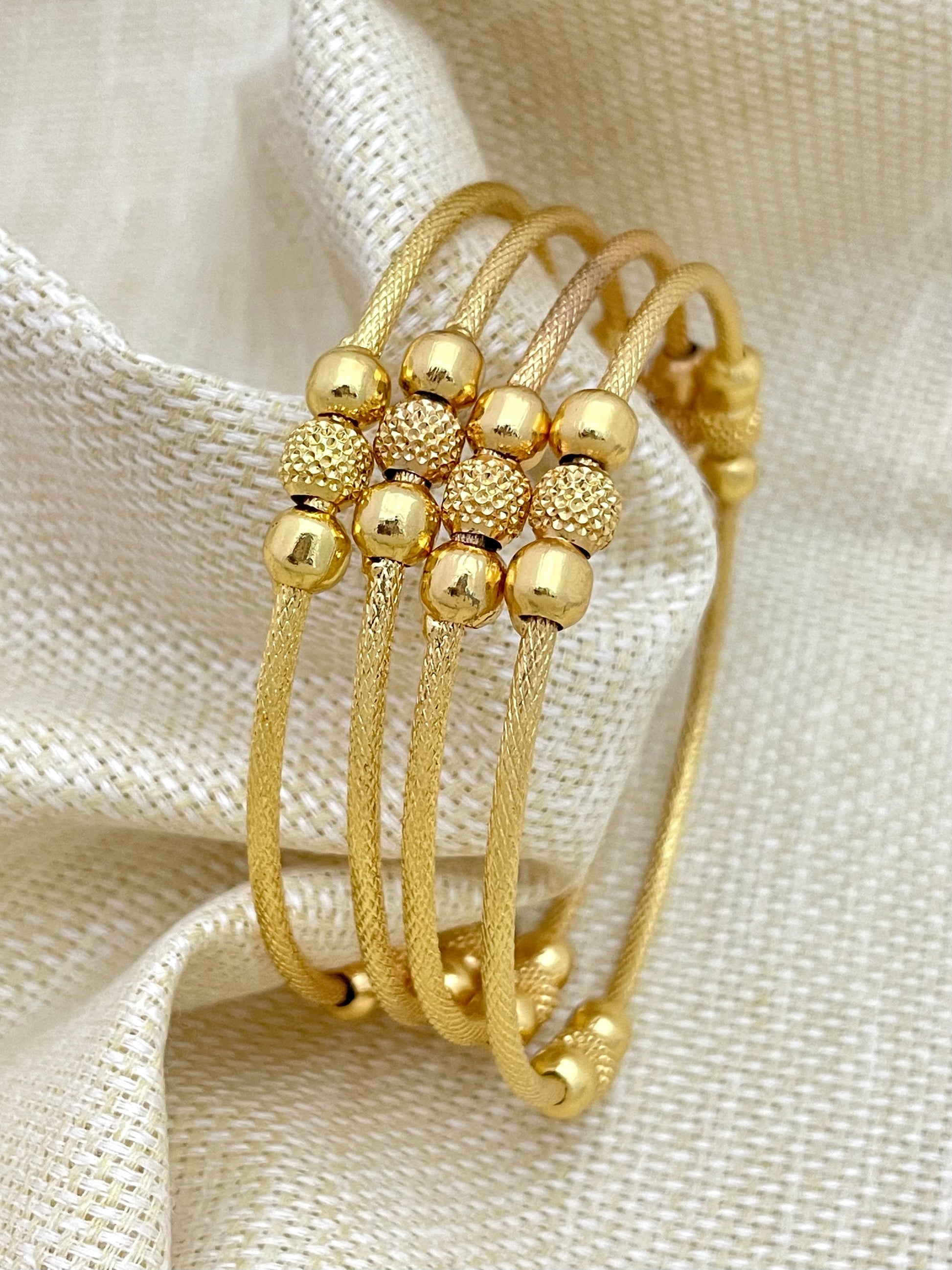 Gold bangles with textured and smooth beads.