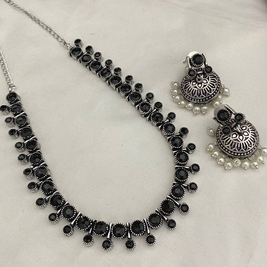 A silver necklace with black circular stones and matching silver earrings with black stones and pearl accents.